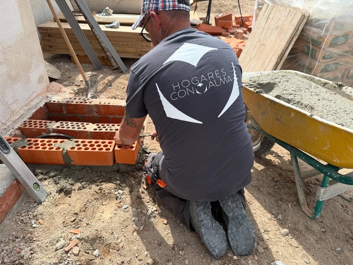 Operario del equipo de Hogares con Alma levantando un muro de ladrillo en obra